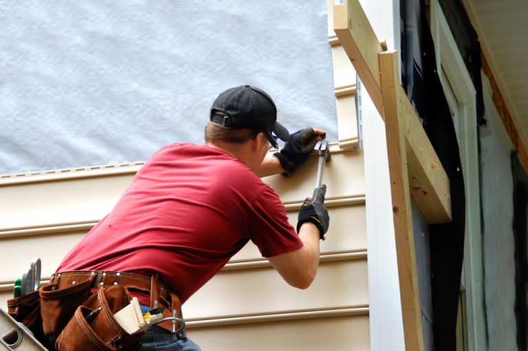 A worker using a hammer working on the exterior of a house