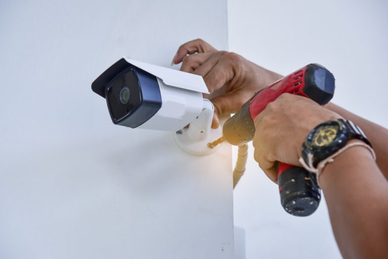 A person installing a security camera using a hand drill