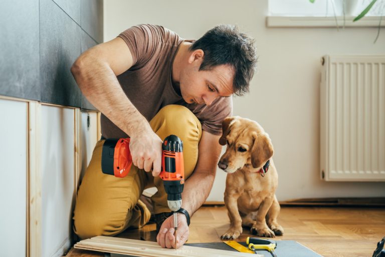 Homebuilder using modern tools while working on a house with a dog watching him work.