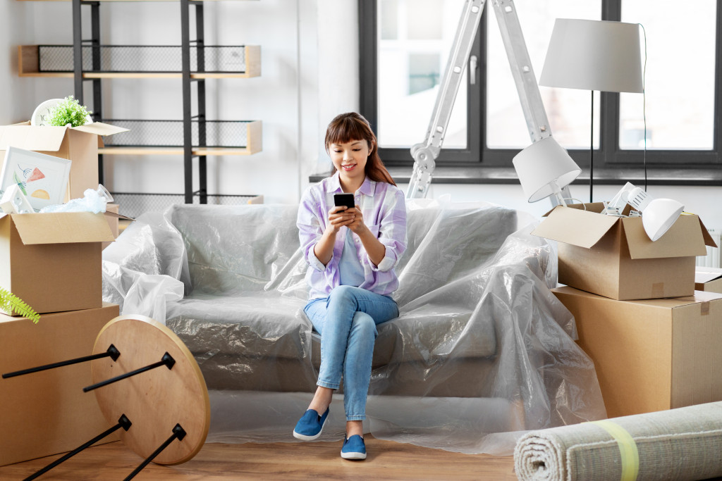 A woman using a phone while sitting on a sofa surrounded by partially unpacked moving boxes